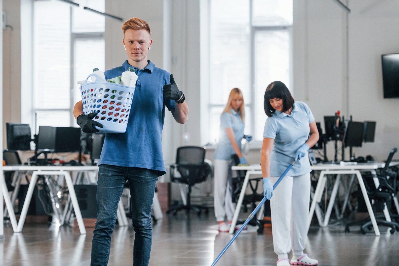 Man holds basket. Group of workers clean modern office together at daytime.