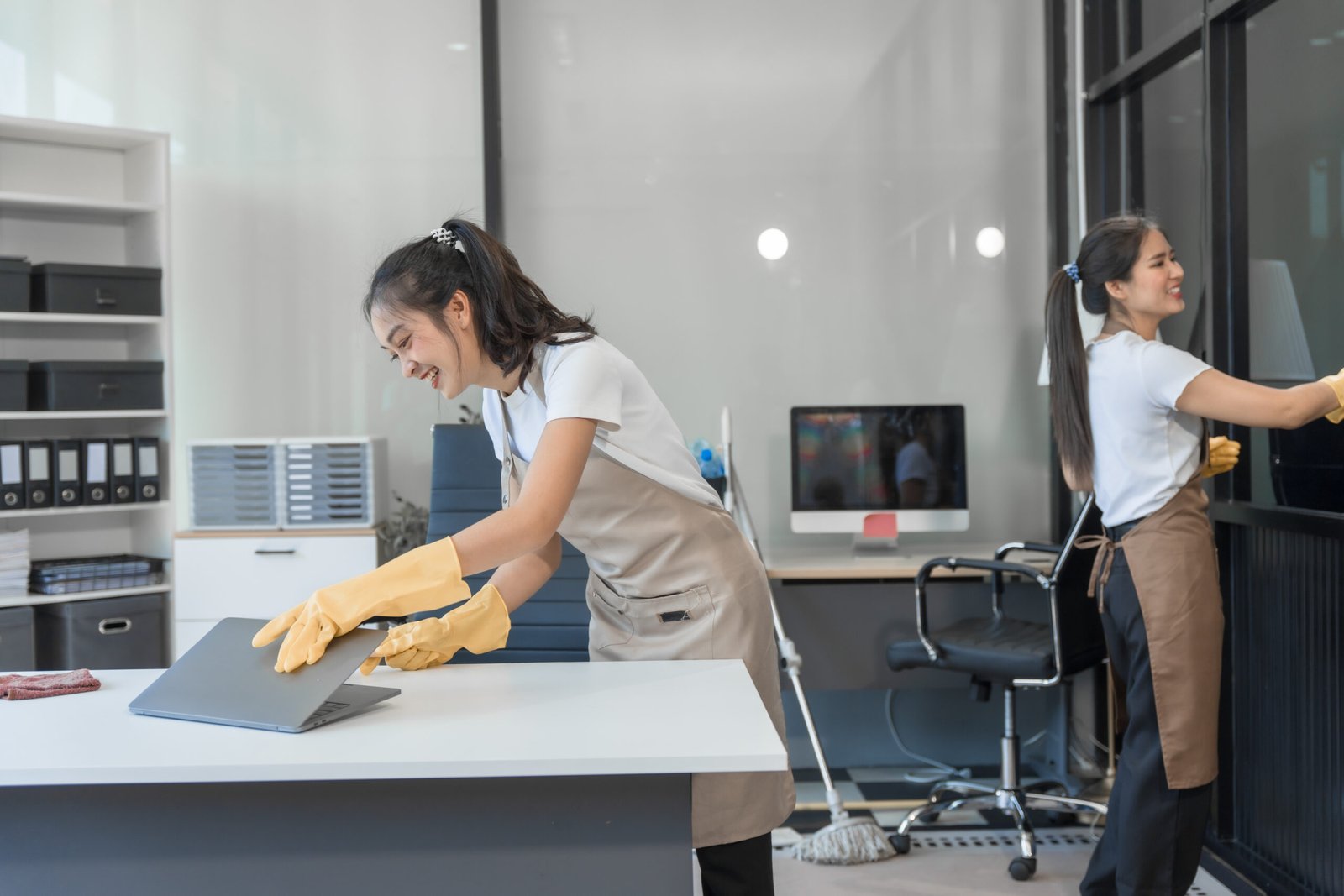 Two Asian housekeepers wear overalls and work together efficiently to clean the living room, study